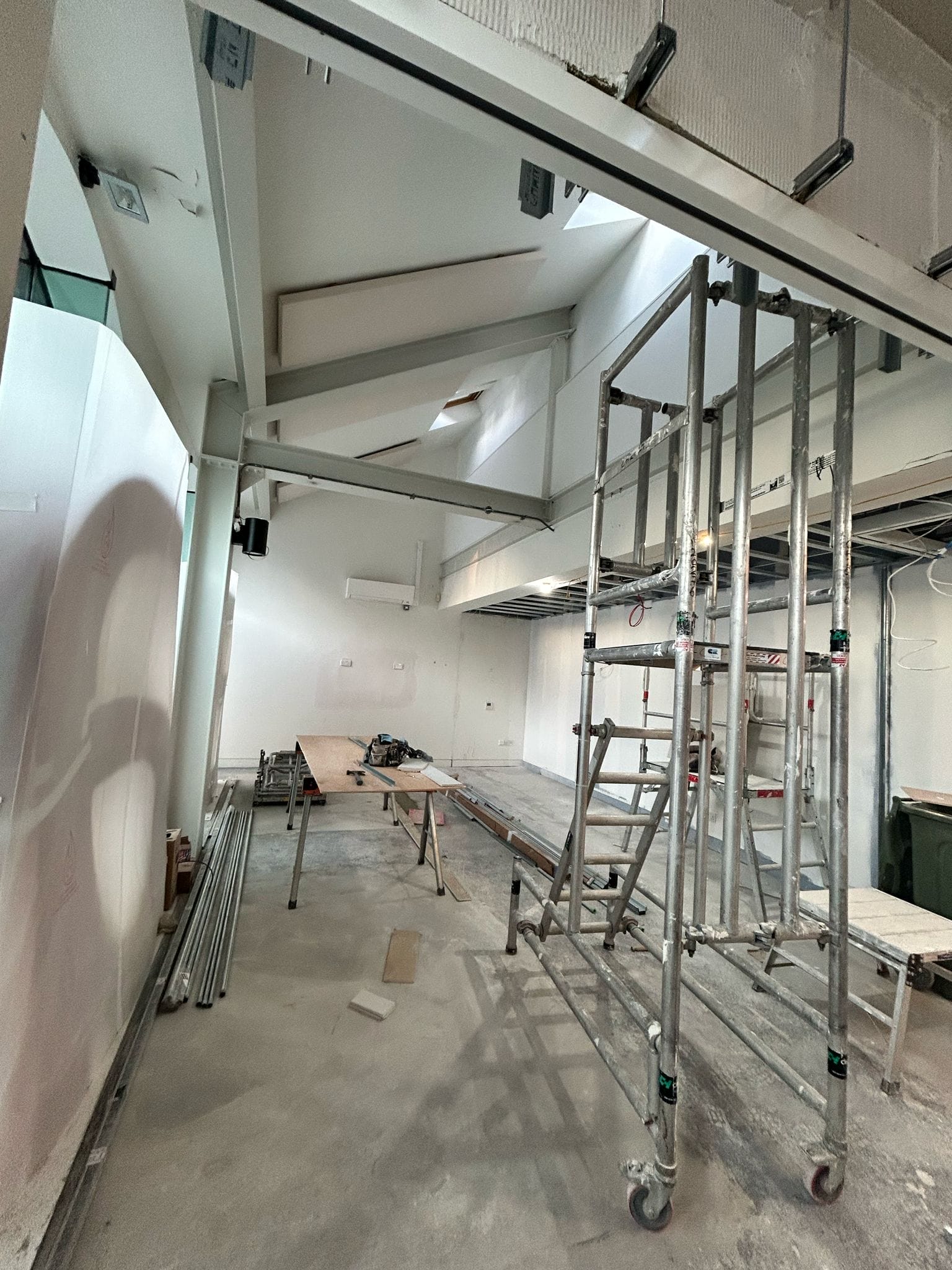 Front lobby of Graeae's building, under construction. New walls have been put up, there are construction materials all around the floor. Light spills in through the window highlighting the giant 